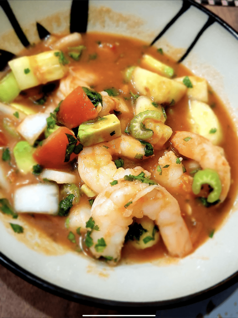 Chilled shrimp gazpacho with ripe avocado and tomato chunks, garnished with cilantro, offering a fresh, zesty flavor.